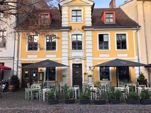 A yellow building with a central door, two outdoor seating areas with umbrellas, and potted plants. - Aparthotel Walhalla (Potsdam)