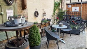 Un espacio al aire libre con mesas y sillas redondas, rodeado de plantas en macetas y una valla de madera.