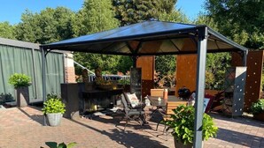 Un patio cubierto con una parrilla, asientos y plantas en macetas.