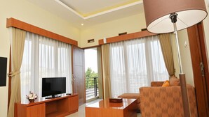 Una sala de estar moderna con televisor de pantalla plana, muebles de madera y ventanas amplias con cortinas.