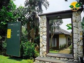 Un arco de piedra que da acceso a un edificio con techo de paja, rodeado de abundante vegetación. Un letrero anuncia la presencia de un restaurante y una cafetería.