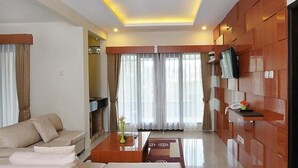 Habitación de hotel moderna con sofá, una mesa de centro, televisor montado en la pared y un ventanal con cortinas.