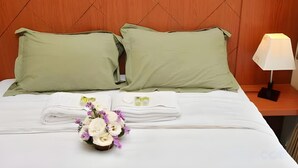 Una cama bien hecha con almohadas verdes, una toalla blanca doblada y un pequeño ramo de flores.