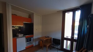 A compact living space with a kitchenette, a small dining table, a TV, and a large window with curtains. - Mini studio with parking in Montgenèvre (Montgenèvre)