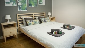 A neatly arranged bedroom with a wooden bed, matching nightstands, and a wall adorned with leaf-patterned artwork. - Warsaw Concierge Family Apartment (Warsaw)