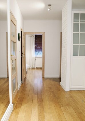 A hallway with wooden flooring, white walls, and a door with frosted glass panels. - Warsaw Concierge Family Apartment (Warsaw)
