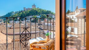 A balcony with a view of a cityscape, including a hill with a castle-like structure.