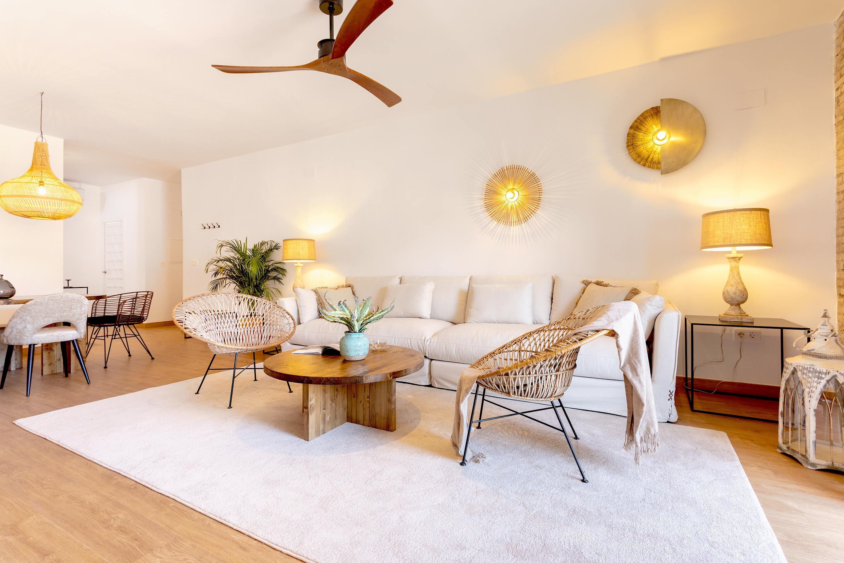 A modern living room with a white sofa, wicker chairs, a wooden coffee table, and a ceiling fan.