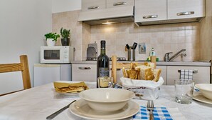 A kitchen with a microwave, a bottle of wine, a basket of bread, and a bowl on the table. - Bilocale Torre delle Ore (Lucca)