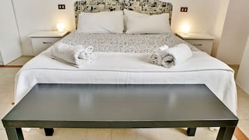 Ein ordentlich bezogenes Bett mit gemustertem Überwurf und Kissen, zwei Nachttische mit Lampen und eine Bank davor.