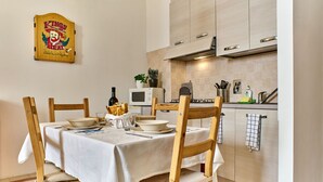 A dining area with a table set for four, wooden chairs, a white tablecloth, and a kitchen in the background with cabinets, a microwave, and a sink. - Bilocale Torre delle Ore (Lucca)