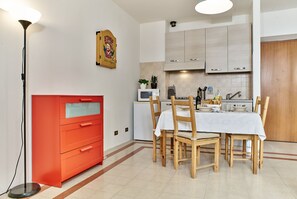 Cocina compacta con una mesa de comedor dispuesta para cuatro personas, un armario rojo, un microondas y un refrigerador pequeño.