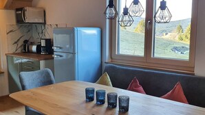 A kitchen with a blue refrigerator, a wooden table, and four glasses. There is a window with a view of a green landscape.
