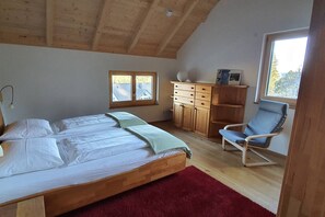 Un dormitorio con una cama de madera, una alfombra roja, un aparador de madera, una silla y una ventana con vistas a árboles.