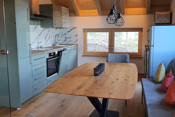 Una cocina moderna con salpicadero de mármol, mesa de madera y vistas al exterior a través de amplios ventanales.