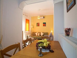 A dining area with a wooden table set for a meal, a fruit basket, and a candle.