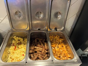 Un bufé con tres secciones que ofrecen huevos revueltos, salchichas y patatas en cubos.