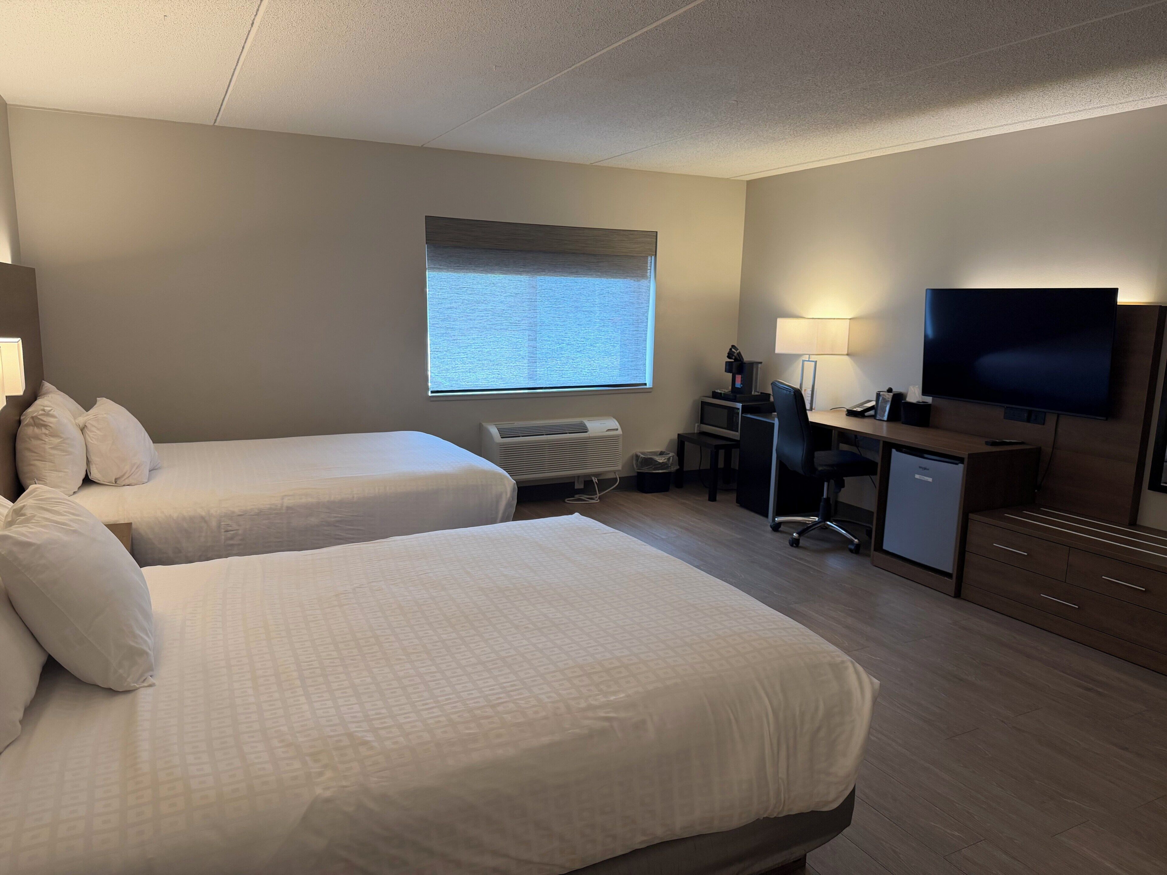 A hotel room with two beds, a desk with a computer, a television, and a window with a view.