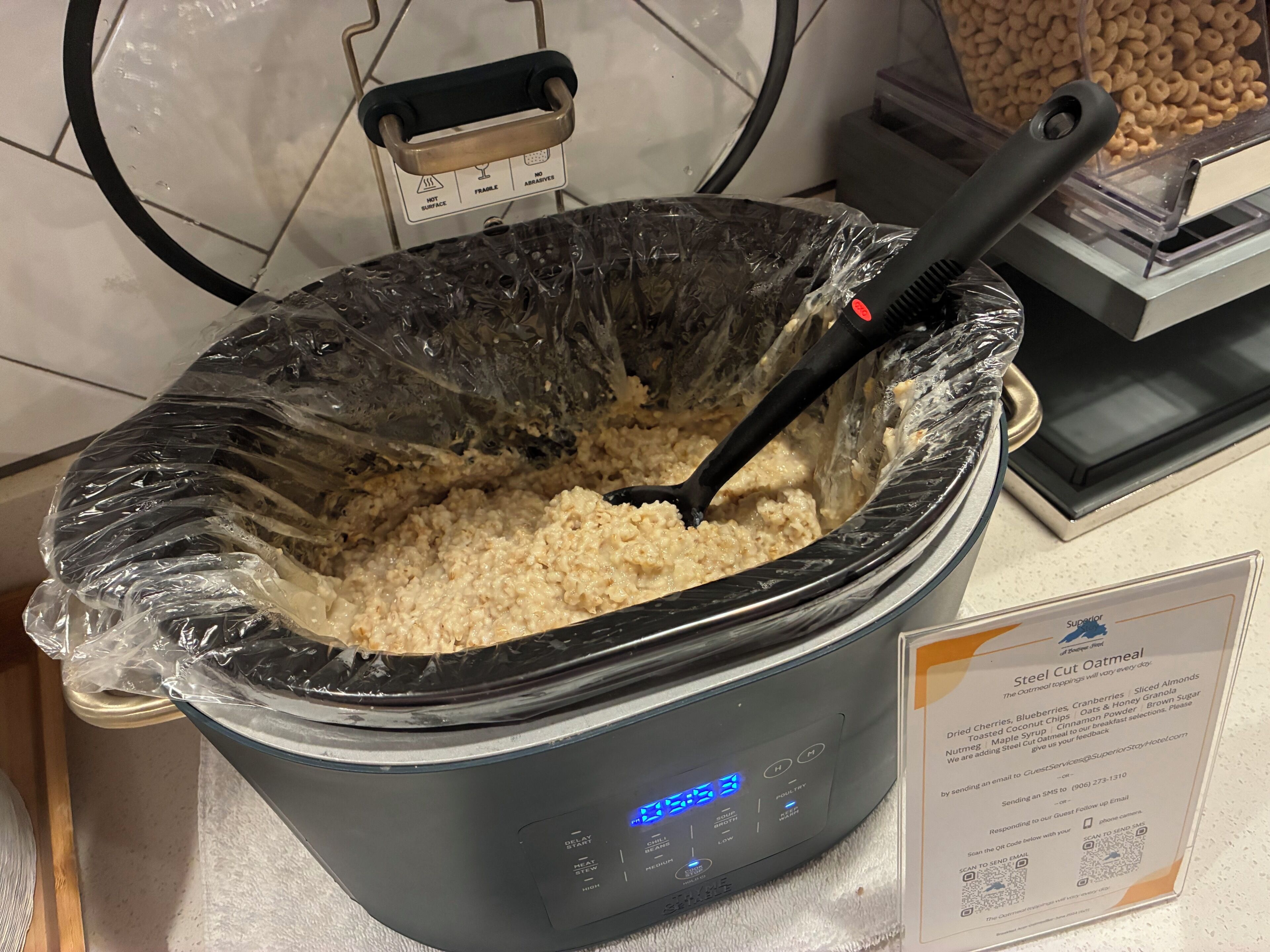 A slow cooker with a plastic cover and a black utensil inside, placed on a kitchen counter.