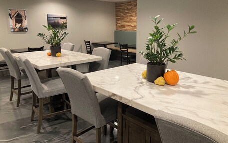 A dining area with marble tables and grey upholstered chairs, featuring potted plants and decorative pumpkins.