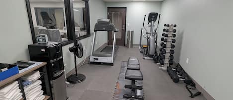 Un área de fitness con cinta de correr, elíptica y mancuernas.