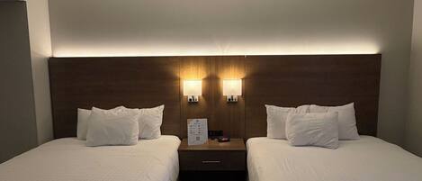 Habitación de hotel con dos camas, cabecero de madera, dos lámparas de pared y una mesita de noche con un reloj.