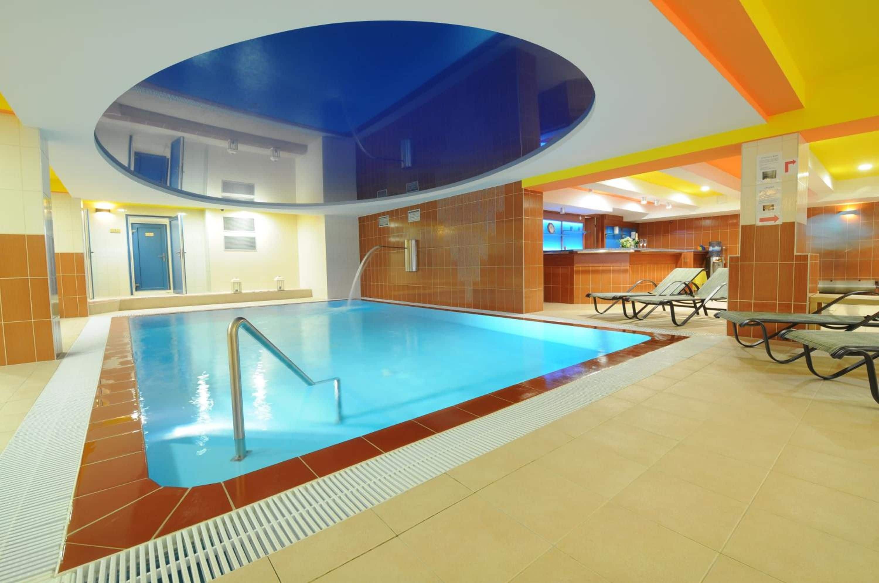 Una piscina interior con superficie de agua cristalina, una escalera de piscina y suelo de baldosas.