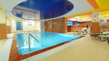 Una piscina interior con superficie de agua cristalina, una escalera de piscina y suelo de baldosas.