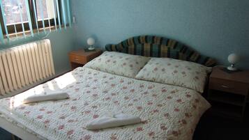A bedroom with a bed, two bedside tables, a radiator, and a window with blinds.