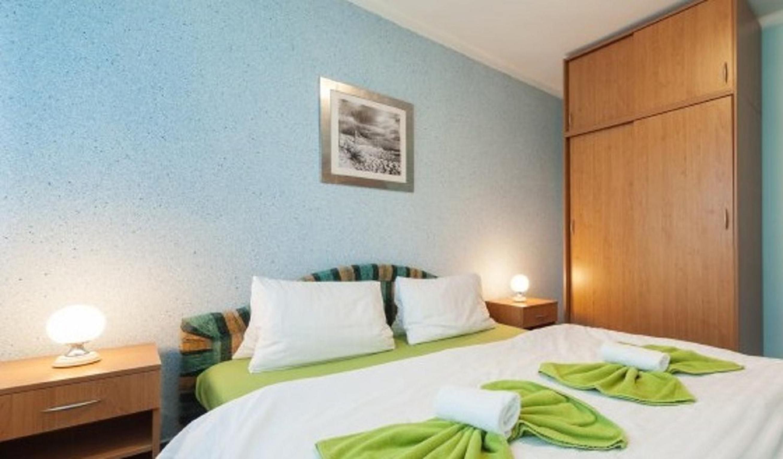 Habitación de hotel con cama, dos mesitas de noche con lámparas, un armario y un cuadro en la pared.