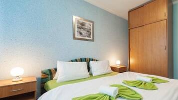 Habitación de hotel con cama, dos mesitas de noche con lámparas, un armario y un cuadro en la pared.