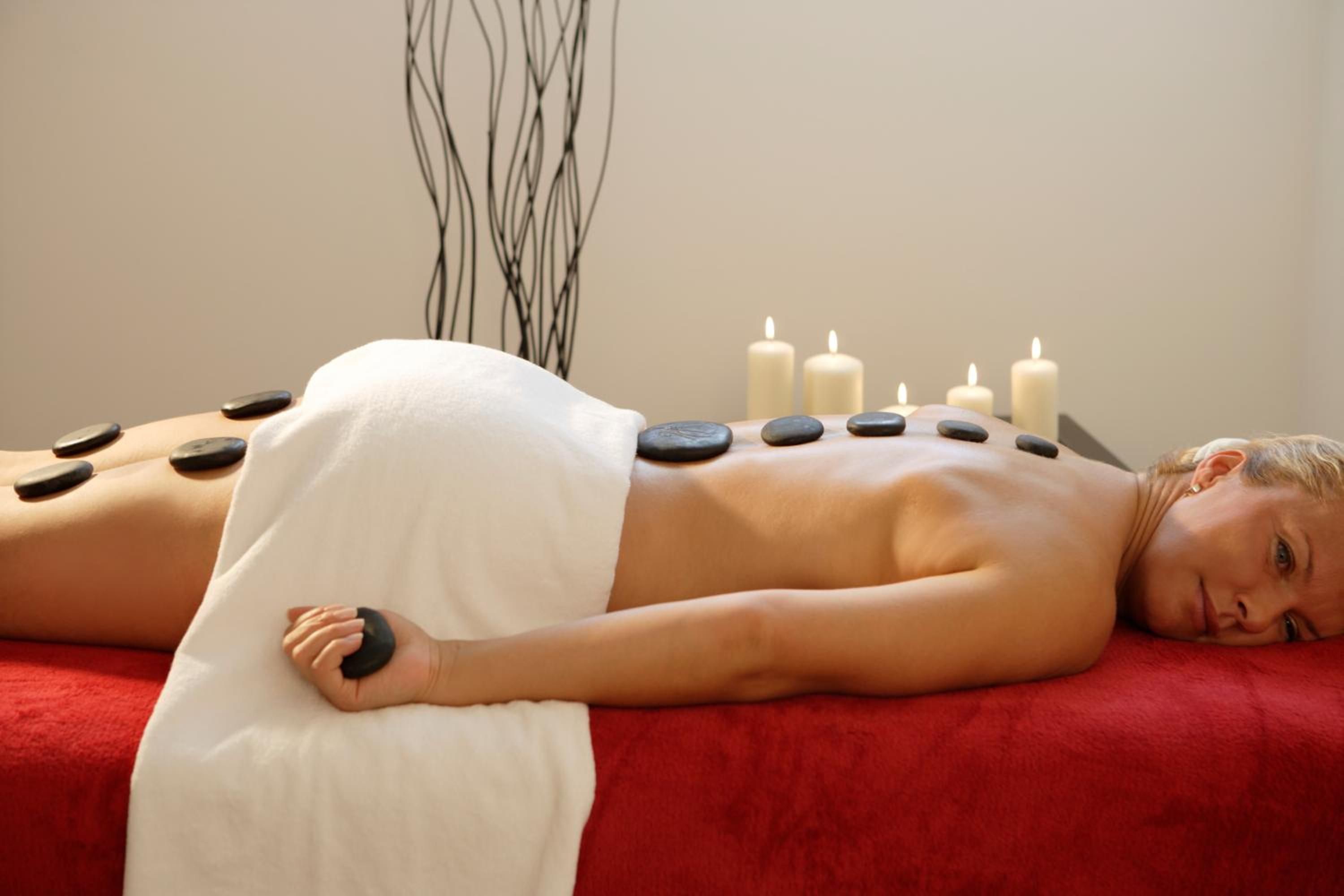 A person receiving a hot stone massage with stones placed on their back, surrounded by candles.