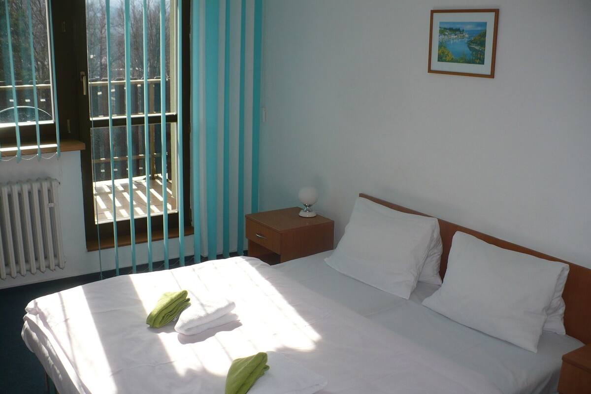 A hotel room with a bed, a nightstand, a window with curtains, and a framed picture on the wall.