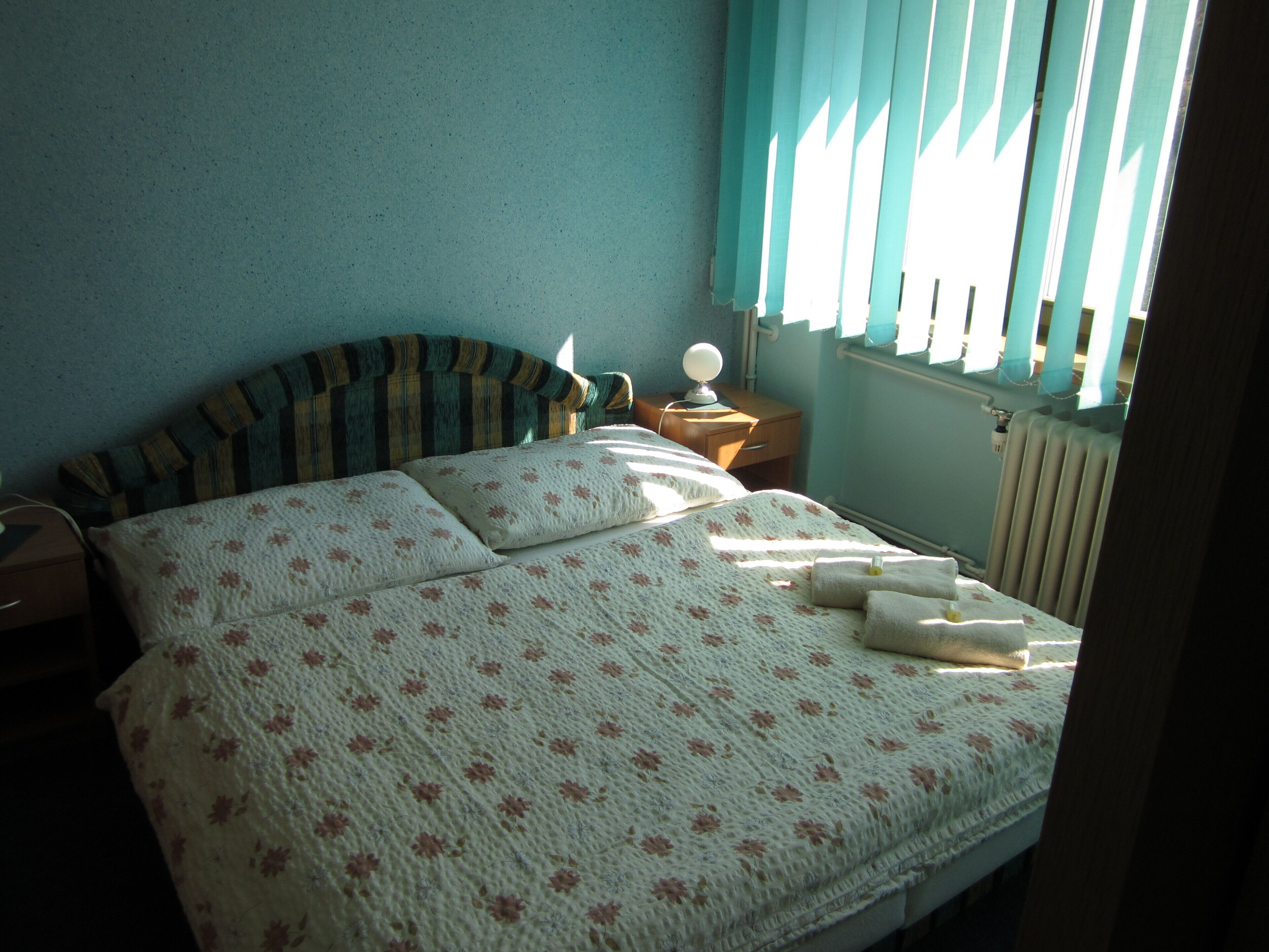 A bed with floral bedding, a bedside lamp, and a window with blinds.