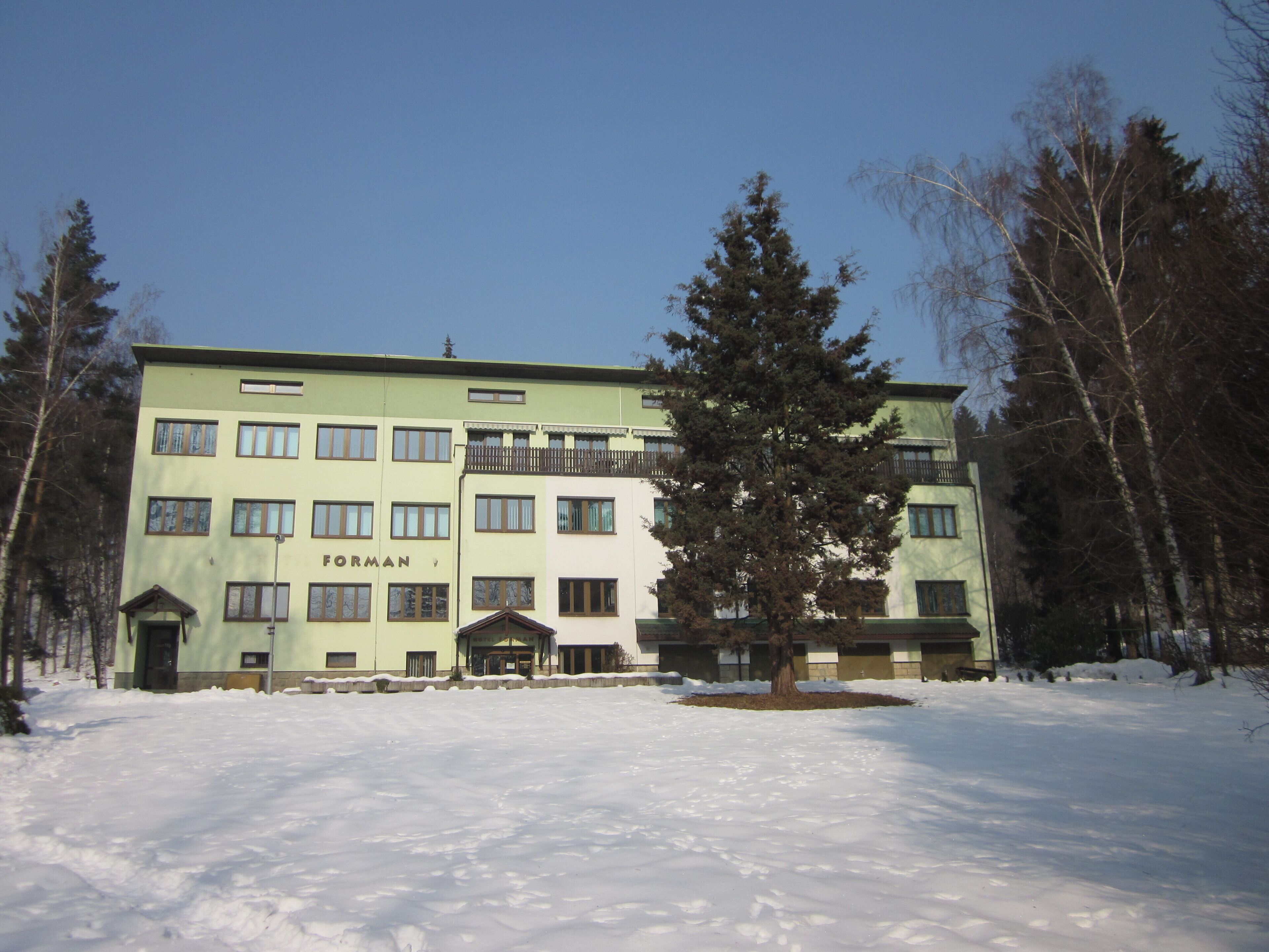 Um edifício de vários andares com a inscrição "FORMAN" na fachada, rodeado por neve e árvores.