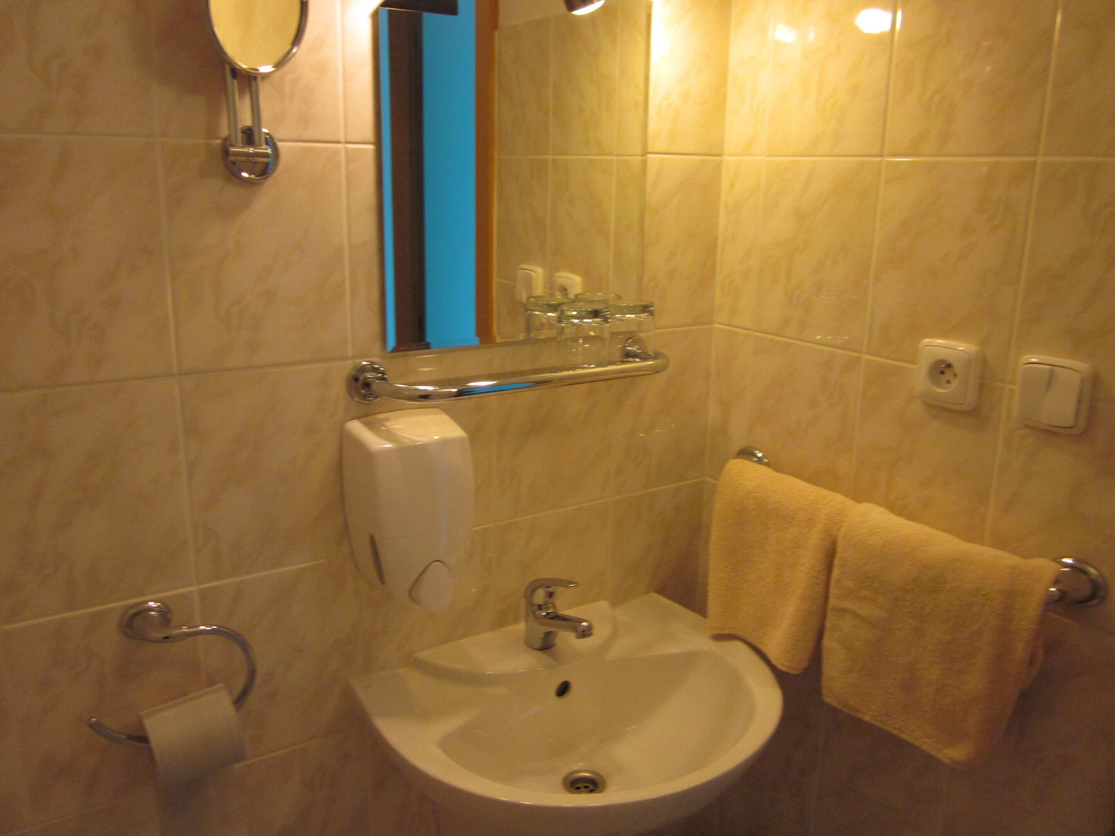 Un baño con lavamanos, espejo, toallero y secador de manos.