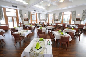 A spacious dining area with multiple tables and chairs, large windows with curtains, and a high ceiling with recessed lighting. - Penzion Forman (Roznov Pod Radhostem)