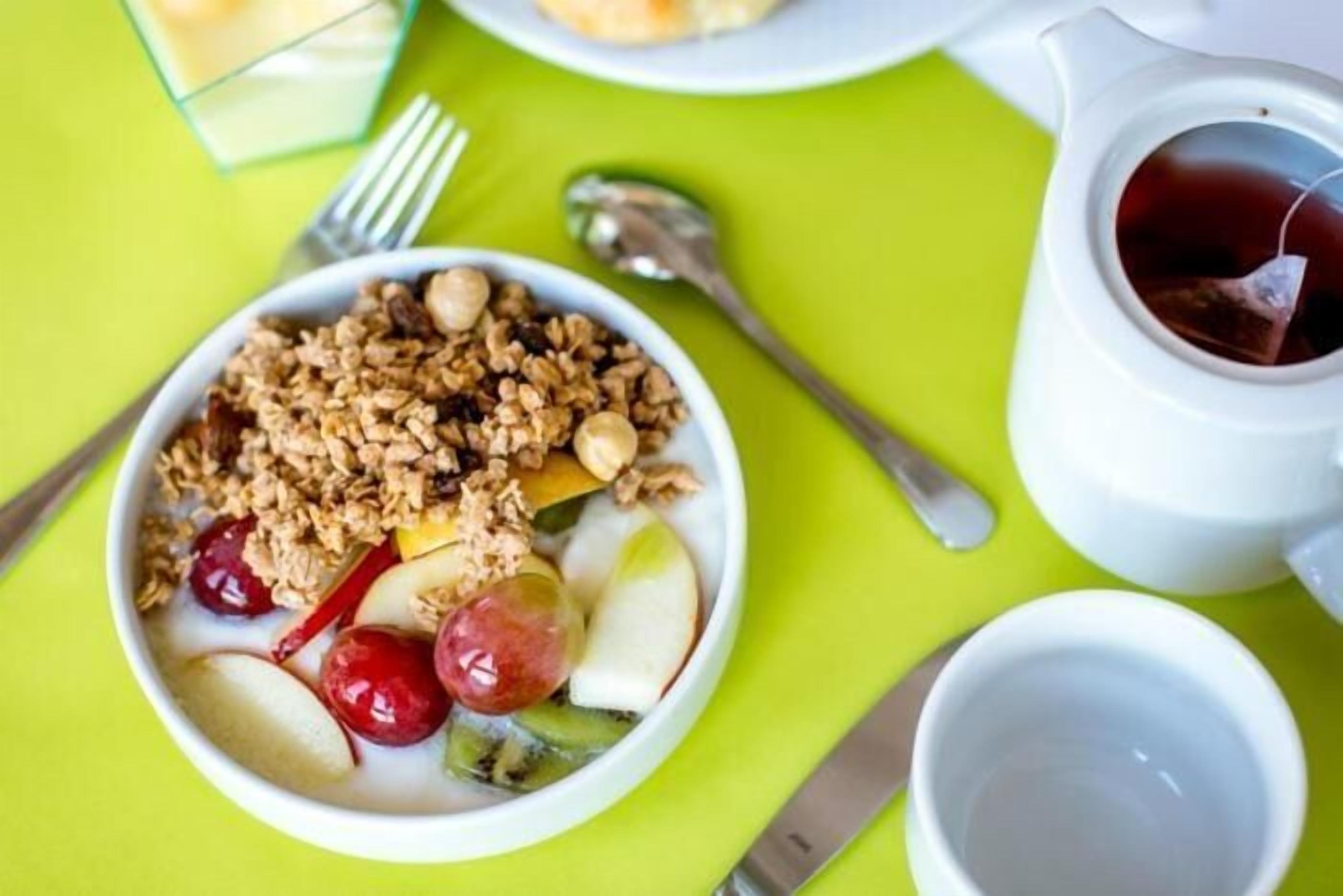 Un tazón de cereal con frutas y nueces sobre una mesa verde.
