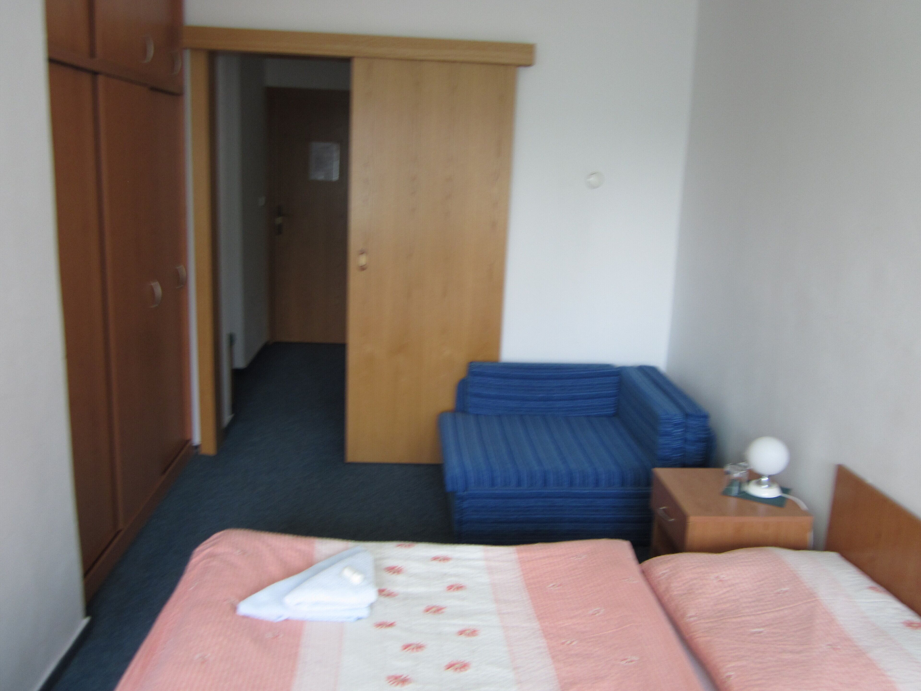Un dormitorio con una cama, un sofá azul, un armario de madera y una puerta que da a otra habitación.