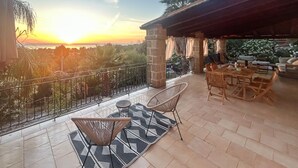 A terrace with a table and chairs, a view of the sunset, and a covered area with seating. - Cozy home in Makari-S. Vito Lo Capo (Makari-S. Vito Lo Capo)