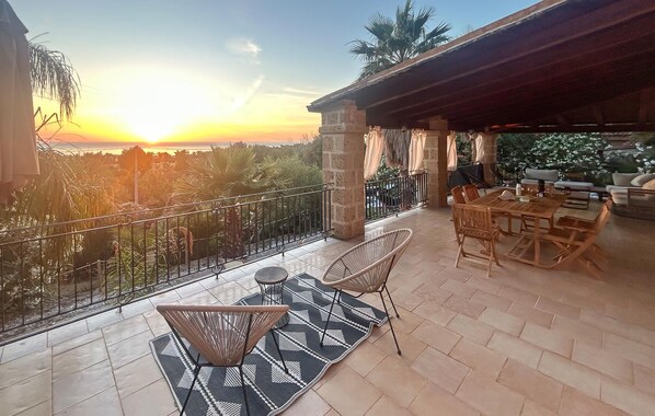 Une terrasse avec une table et des chaises, une vue sur le coucher de soleil et un espace abrité avec des sièges.