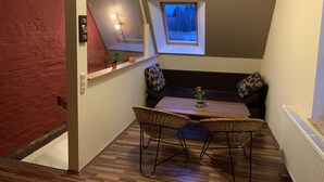 Una habitación acogedora con suelo de madera, una mesita con dos sillas, una ventana con vistas a árboles y una pared de ladrillo rojo.