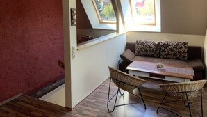 Una habitación acogedora con techo alto, un sofá con cojines estampados, una mesita y dos sillas de mimbre.