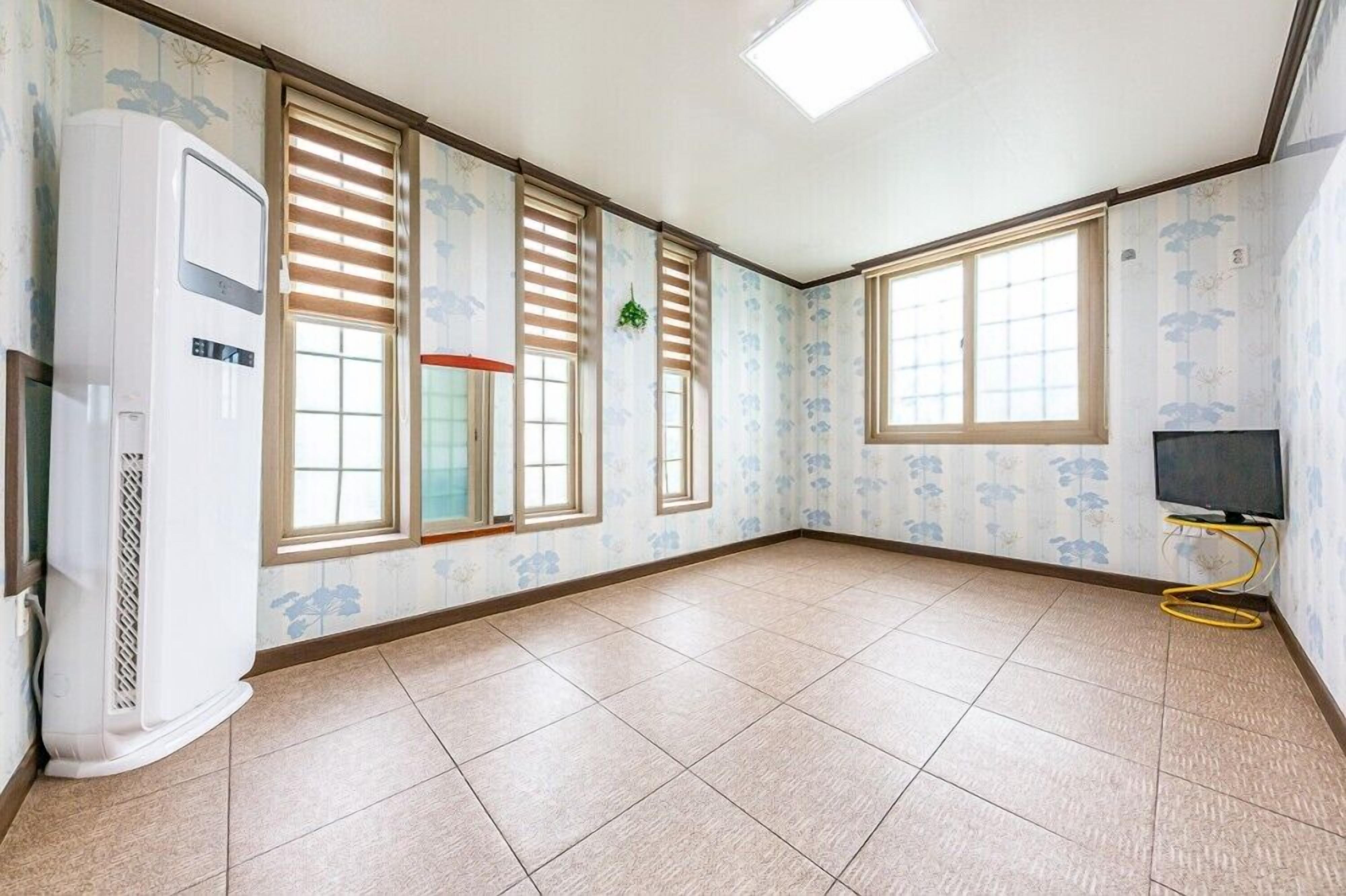 A spacious room with large windows, a built-in air conditioner, and a flat-screen TV on a stand.