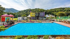 Une piscine entourée de chaises longues aux couleurs vives et un bâtiment à la façade jaune et violette.