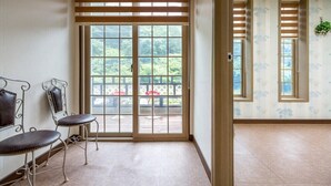 Une pièce dotée d’une grande porte-fenêtre coulissante donnant sur un espace extérieur avec une terrasse en bois et des chaises.