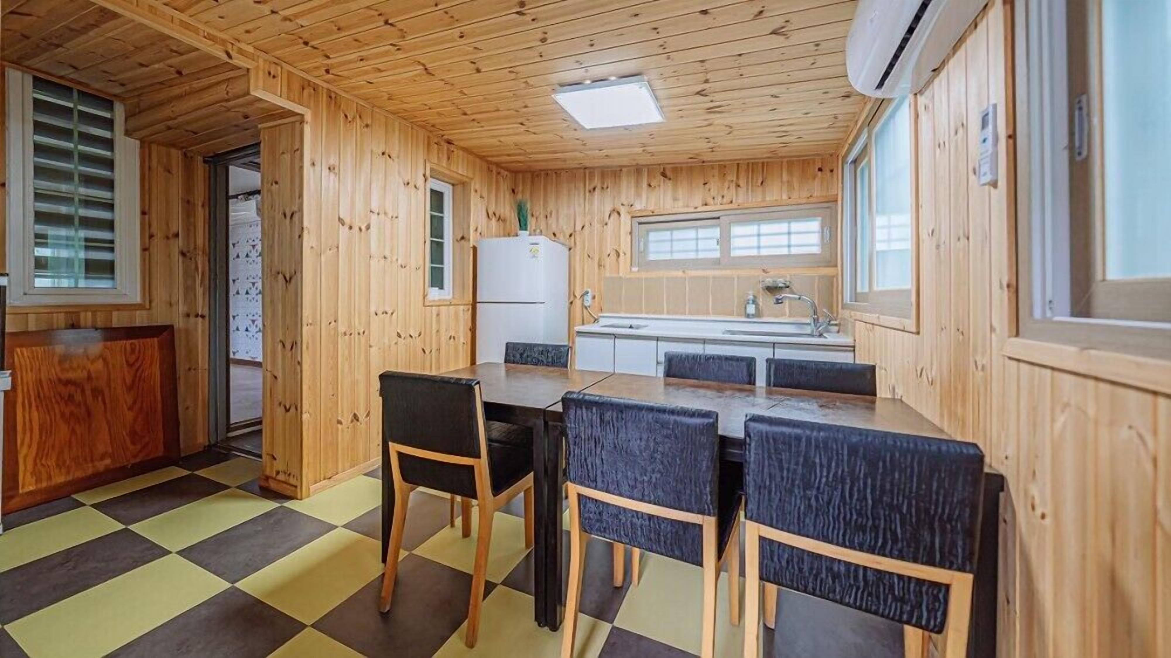 A wooden cabin interior with a kitchen, dining area, and a large window.