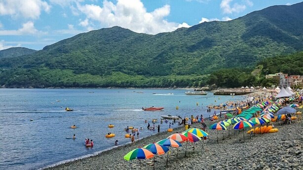 Une plage avec des parasols colorés, où l’on peut voir des gens nager et prendre des bains de soleil.
