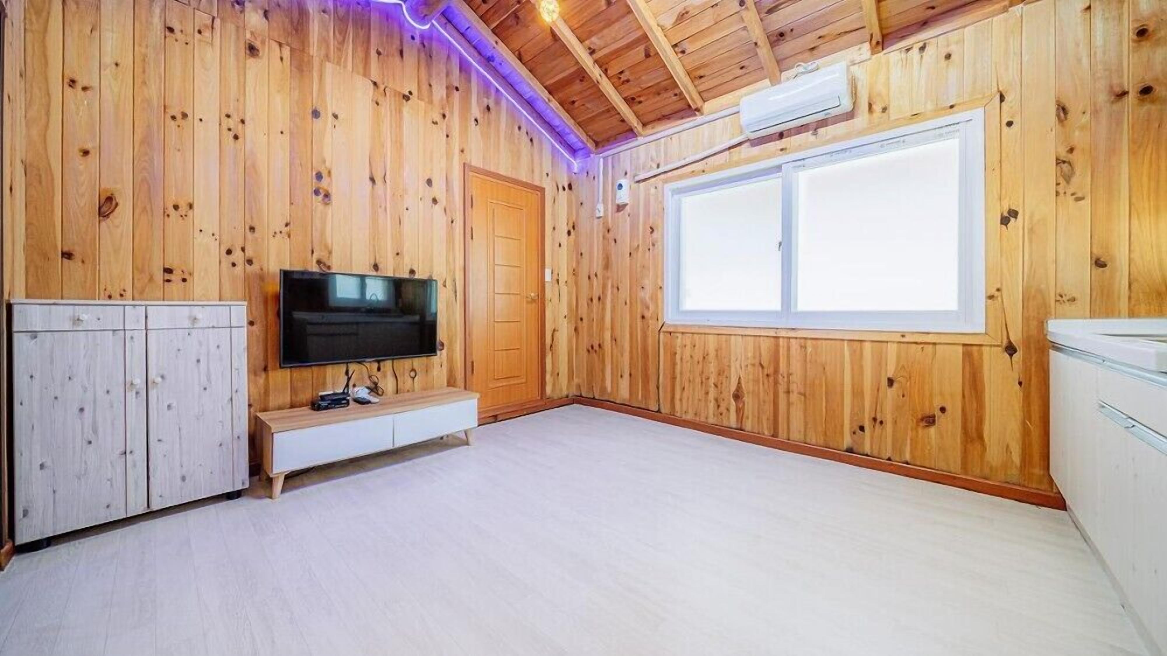 A room with wooden walls, a large window, a television, and a white cabinet.