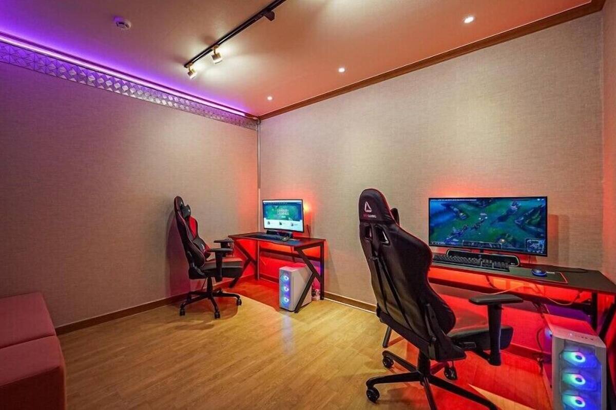A gaming room with two gaming stations, each with a monitor, chair, and illuminated red desk.